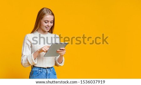 App For Students. Beautiful teen girl using digital tablet over orange studio background, panorama with copy space