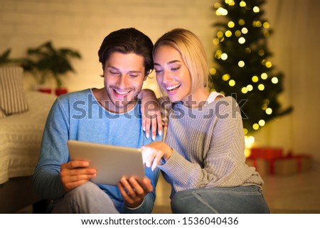 Couple looking at old photos on tablet, sitting next to Christmas tree