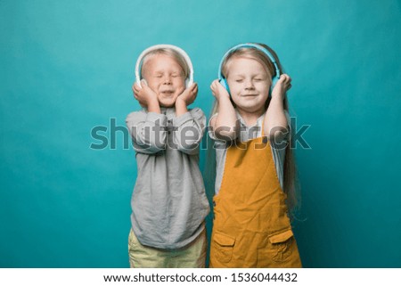 Very emotional children listen to music with headphones on a blue background. Boy and girl are dancing and showing different emotions and he is happy