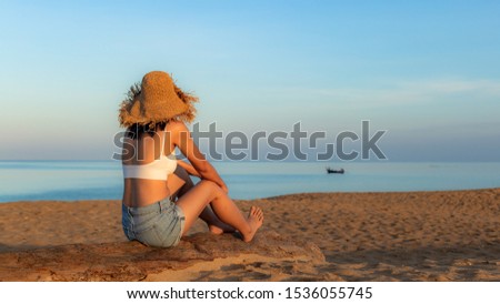 Young and beautiful woman wearing a hat in sunrise light looking far away, Photo from behind.