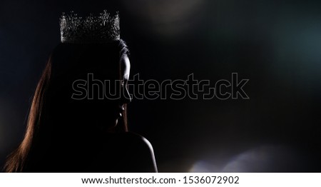 Portrait of Miss Pageant Beauty Contest in sequin Evening Ball Gown long dress with sparkle light Diamond Crown, silhouette low key exposure with curtain, studio lighting dark background dramatic