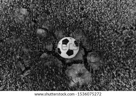 A black and white picture of a football ball on a dry and cracked soil field.