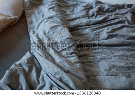 A gray cotton sheet and blankets with pillows on the bed