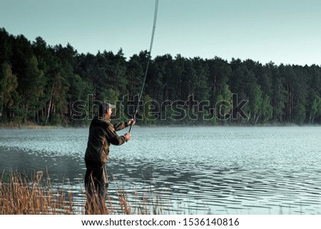 A male fisherman on the lake is standing in the water and fishing for a fishing rod. Fishing hobby vacation concept. Copy space