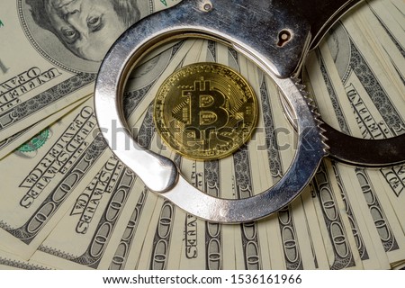 Handcuffs on hundred dollar bills and a gold bitcoin coin. Close-up