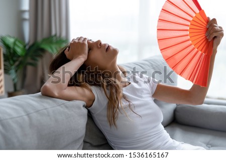 Side view exhausted young biracial girl using paper waver, suffering from hot summer weather or high temperature at home. Unhappy overheated millennial mixed race woman feeling uncomfortable indoors. Royalty-Free Stock Photo #1536165167