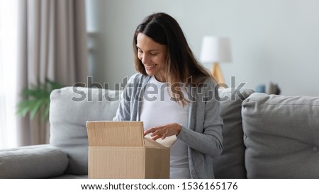 Smiling young mixed race female customer unpacking carton box, looking inside, happy get wished item order from internet store. Positive client satisfied with trusted company fast shipment delivery. Royalty-Free Stock Photo #1536165176