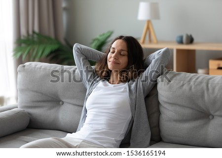 Tranquil smiling biracial millennial woman leaning on sofa, enjoying stress free weekend time at home. Mindful happy mixed race young girl relaxing in living room, meditating, visualizing future. Royalty-Free Stock Photo #1536165194