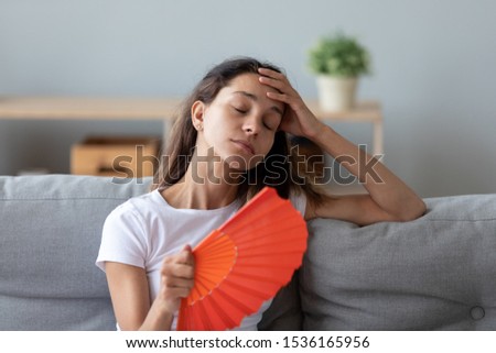 Head shot unhappy millennial mixed race woman suffering from high temperature at home, using paper fan. Overheated young girl cooling herself, feeling uncomfortable without air conditioning indoors. Royalty-Free Stock Photo #1536165956