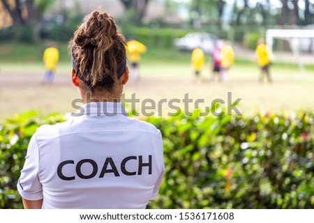 Back view of a female soccer, football, coach in white coach shirt watching her team play at an outdoor football field Royalty-Free Stock Photo #1536171608