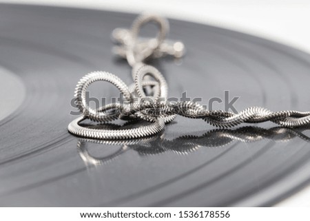 A silver chain with an elegant design is twisted into rings and lies on a black vinyl record