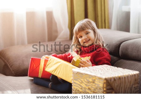Cute child girl in a red sweater with Christmas gift boxes at home
