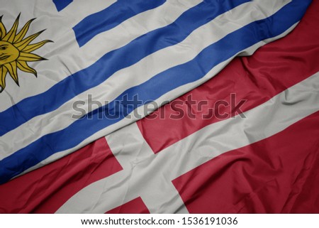 waving colorful flag of denmark and national flag of uruguay. macro