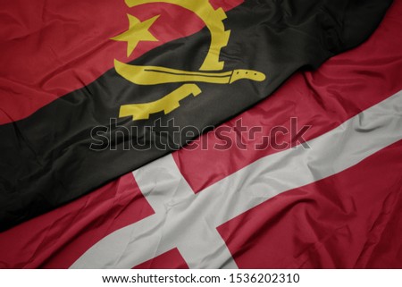 waving colorful flag of denmark and national flag of angola. macro