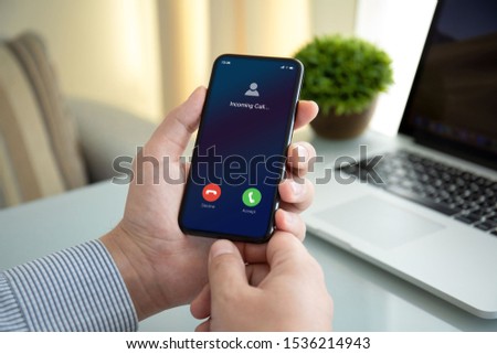 male hands holding phone with incoming call on the screen above table in office Royalty-Free Stock Photo #1536214943