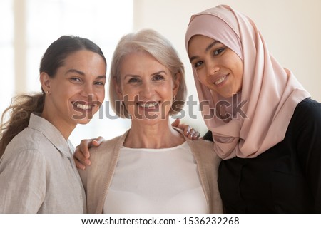 Three happy beautiful diverse two generation women young asian muslim woman wear hijab and caucasian older mature female multicultural ladies bonding standing together looking at camera, portrait Royalty-Free Stock Photo #1536232268