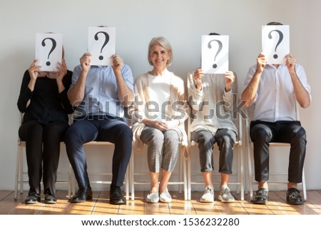 Happy hired employed mature old businesswoman professional chosen candidate sitting among people hiding faces behind questions marks waiting for job interview, human resource, recruit choice concept Royalty-Free Stock Photo #1536232280