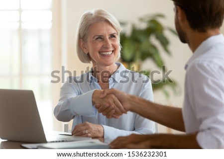 Smiling old mature saleswoman handshake businessman client customer hire job candidate at employment business meeting, happy middle aged bank manager sell loan insurance service shake customer hand Royalty-Free Stock Photo #1536232301