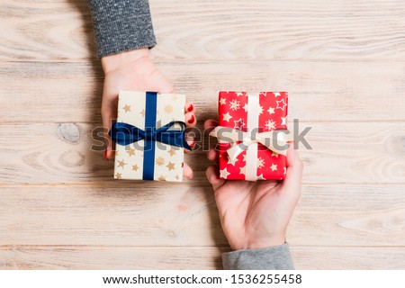 Top view of a woman and a man exchanging gifts on wooden background. Couple give presents to each other. Close up of making surprise for holiday concept.