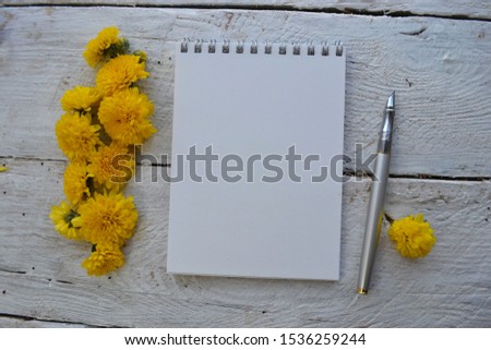 Empty sketchbook on wooden desk with yellow flowers and pen. Mockup for elegant design with space for text.