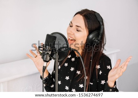 Beautiful woman in headphones sings a song near a microphone in a recording studio. Place for text or advertising