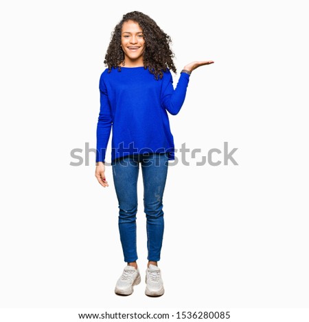 Young beautiful woman with curly hair wearing winter sweater smiling cheerful presenting and pointing with palm of hand looking at the camera.