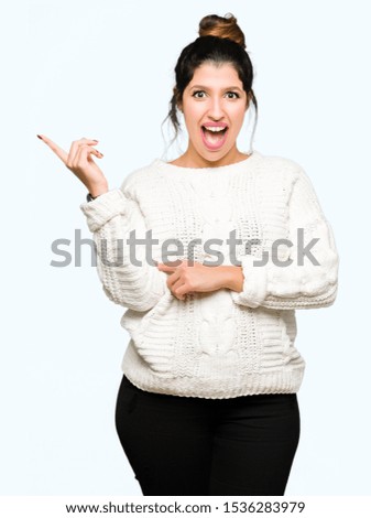 Young beautiful woman wearing winter sweater with a big smile on face, pointing with hand and finger to the side looking at the camera.