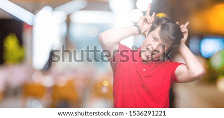 Young handsome man wearing red t-shirt over isolated background Posing funny and crazy with fingers on head as bunny ears, smiling cheerful