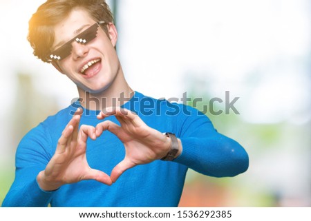 Young man wearing funny thug life glasses over isolated background smiling in love showing heart symbol and shape with hands. Romantic concept.