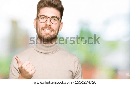 Young handsome business man wearing glasses doing happy thumbs up gesture with hand. Approving expression looking at the camera showing success.