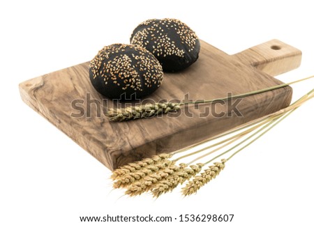 Black round bread sprinkled with sesame seeds on a cutting board with spikelets on a white background