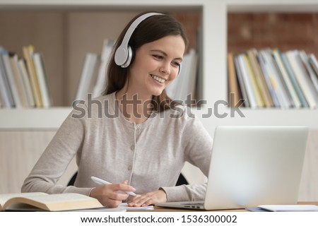 Girl sitting at desk wearing headphones look at pc screen noting learning studying in library, woman take online classes improve english knowledge or preparing for exam with friend distantly concept Royalty-Free Stock Photo #1536300002