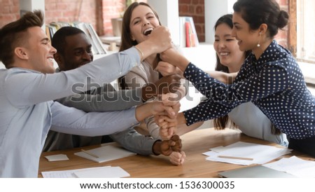 Group of multi-ethnic students seated at classroom desk put their fists on top of each other laughing showing unity trust, friendly relations, racial equality, successful study accomplishment concept Royalty-Free Stock Photo #1536300035