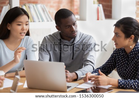 African guy Asian and Indian girls do assignment together, multinational trainees group listens challenge solutions of team leader, teamwork, help at learning process high school participants concept Royalty-Free Stock Photo #1536300050