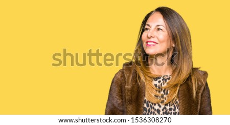 Beautiful middle age elegant woman wearing mink coat looking away to side with smile on face, natural expression. Laughing confident.