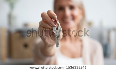 Happy senior middle aged woman customer landlord hold key to new house apartment give to camera, older retired female hand real estate owner make sale purchase property deal concept, close up view Royalty-Free Stock Photo #1536338246