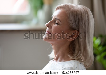 Calm serene middle aged woman meditating with eyes closed inhaling fresh air relaxing indoors, happy healthy old mature lady enjoying resting feel peace of mind doing breathing yoga exercises at home Royalty-Free Stock Photo #1536338297