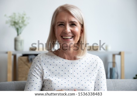 Happy mature old woman blogger looking at camera at home, smiling middle aged senior lady sit on sofa talking by webcam laughing enjoying video conference call online or shooting blog vlog at home Royalty-Free Stock Photo #1536338483