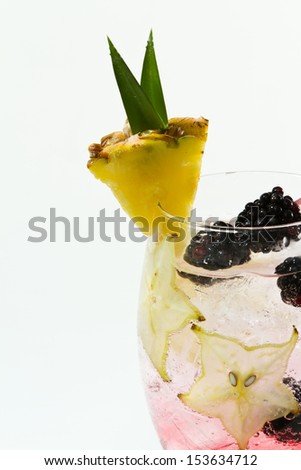 cocktail served in a chalice garnished with a pineapple slice, carambola slices and blackberries isolated on a white background