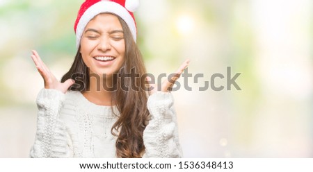 Young arab woman wearing christmas hat over isolated background celebrating mad and crazy for success with arms raised and closed eyes screaming excited. Winner concept