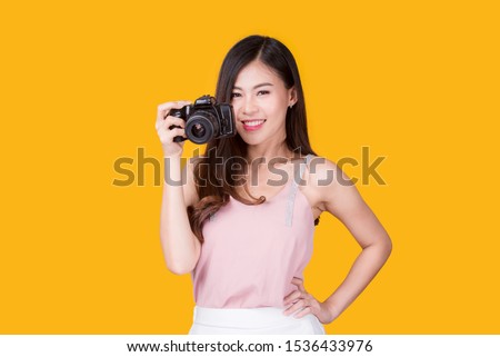 Portrait of a beautiful asian young woman taking picture by digital camera on yellow background. Technology, Camera, Beauty and fashion.