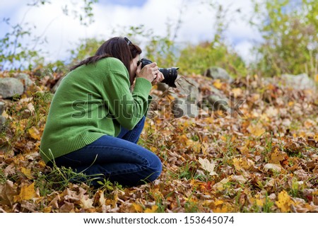 Female photographer crouching in fall leaves to take a picture 