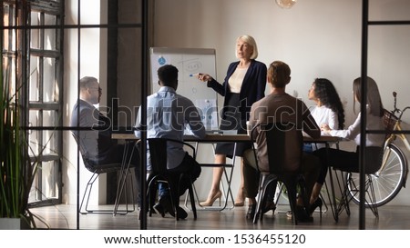 Mature older businesswoman mentor coach training speaker give flip chart business presentation at company meeting, confident female executive manager teaching team consult clients at office workshop Royalty-Free Stock Photo #1536455120