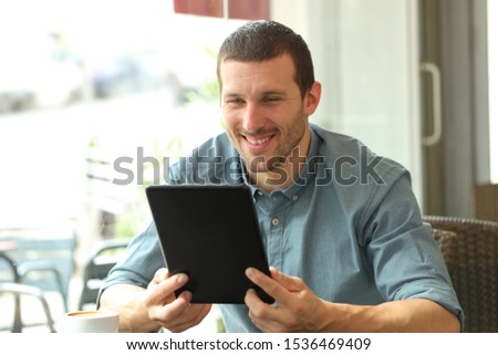 Happy man reading tablet content sitting in a coffee shop