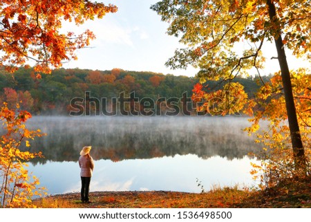 Beautiful Fall Foliage of New England at Sunrise, Boston Massachusetts. Photo shows a tourist standing in front of lake.
