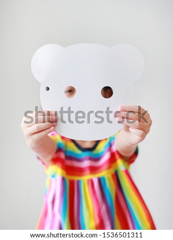 Cute little child girl showing blank white animal paper mask fronting her face on white background. Idea and concept for kid dressed up playing animal face.