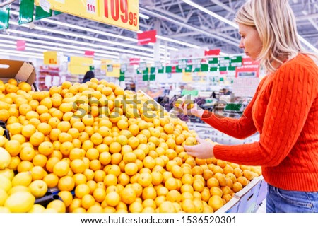 Juicy yellow oranges on a counter in a supermarket. Young woman chooses fruits.