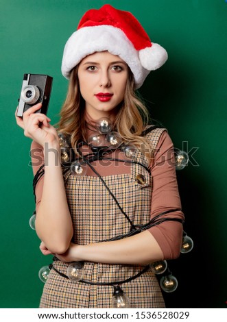 Portrait of a woman with Christmas lights and vintage camera on green background