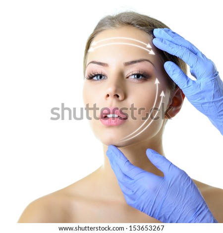facelift, beauty treatment of the young beautiful female face, doctor's hand in gloves touch face of beautiful young woman isolated on white  Royalty-Free Stock Photo #153653267