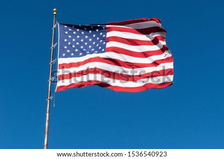 The flag of the Unites States of America against a blue sky on a windy day.